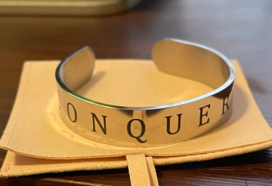 Silver bracelet with 'CONQUEROR' engraving on a beige fabric background