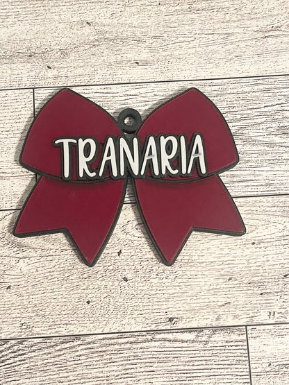 Red cheer bow-shaped backpack tag with text on a wooden surface
