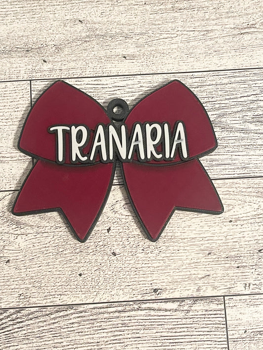 Red cheer bow-shaped backpack tag with text on a wooden surface