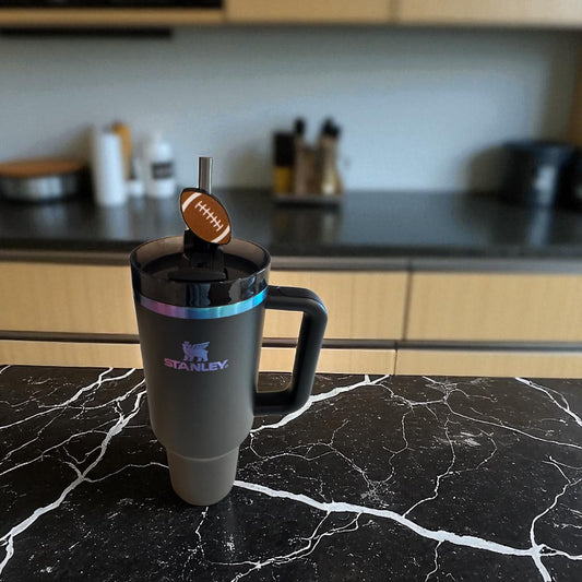 Tumbler with a football-themed straw  topper on a marble countertop in a kitchen.