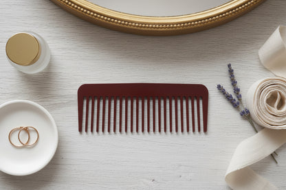 Brown comb on a light surface with a mirror, bottle, and decorative elements.