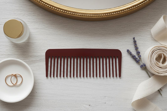 Brown comb on a light surface with a mirror, bottle, and decorative elements.