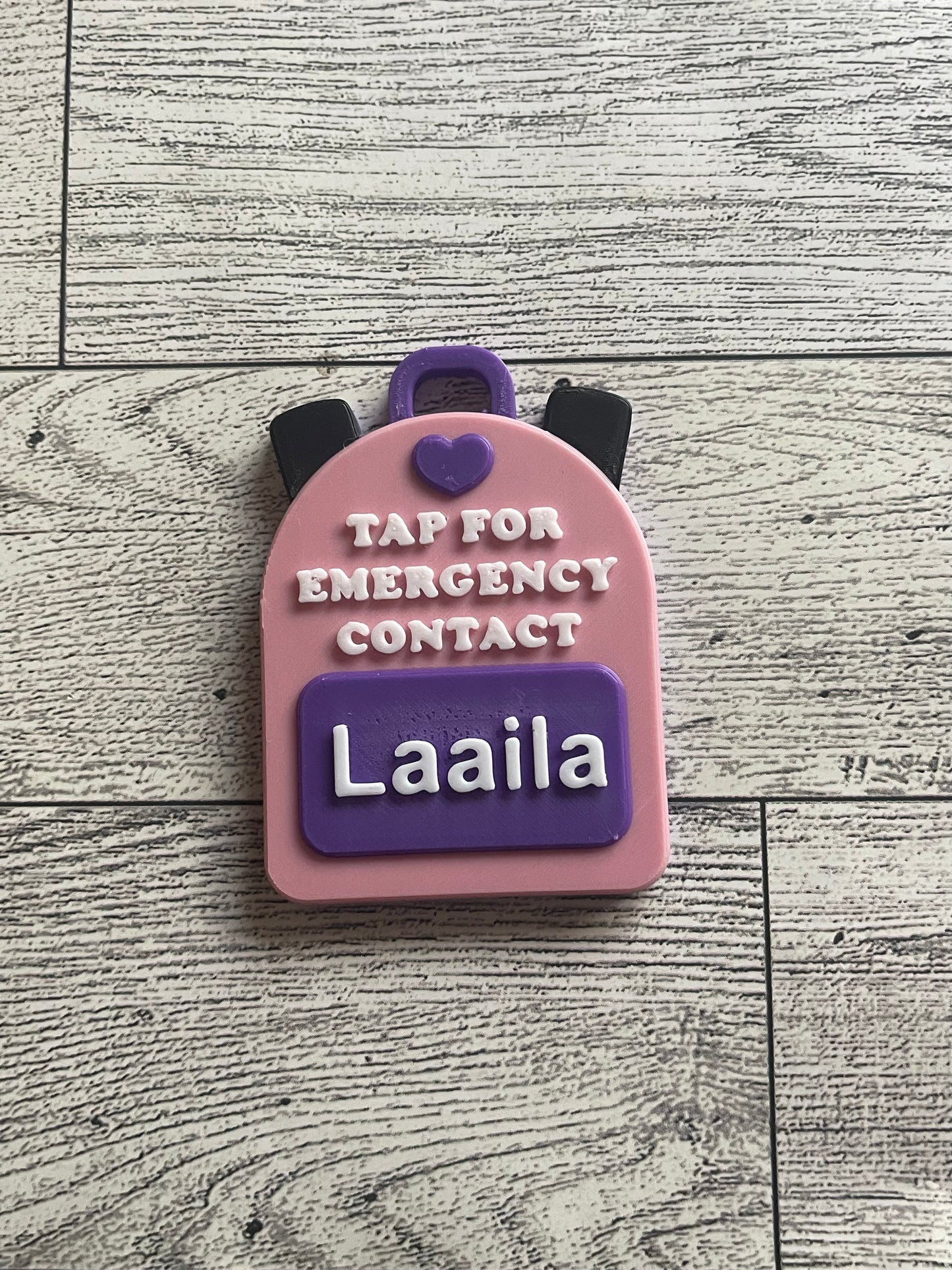 Pink backpack-shaped emergency contact tag with name on a wooden surface