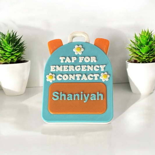 Backpack-shaped emergency contact device with 'Tap for Emergency Contact name text, surrounded by potted plants.