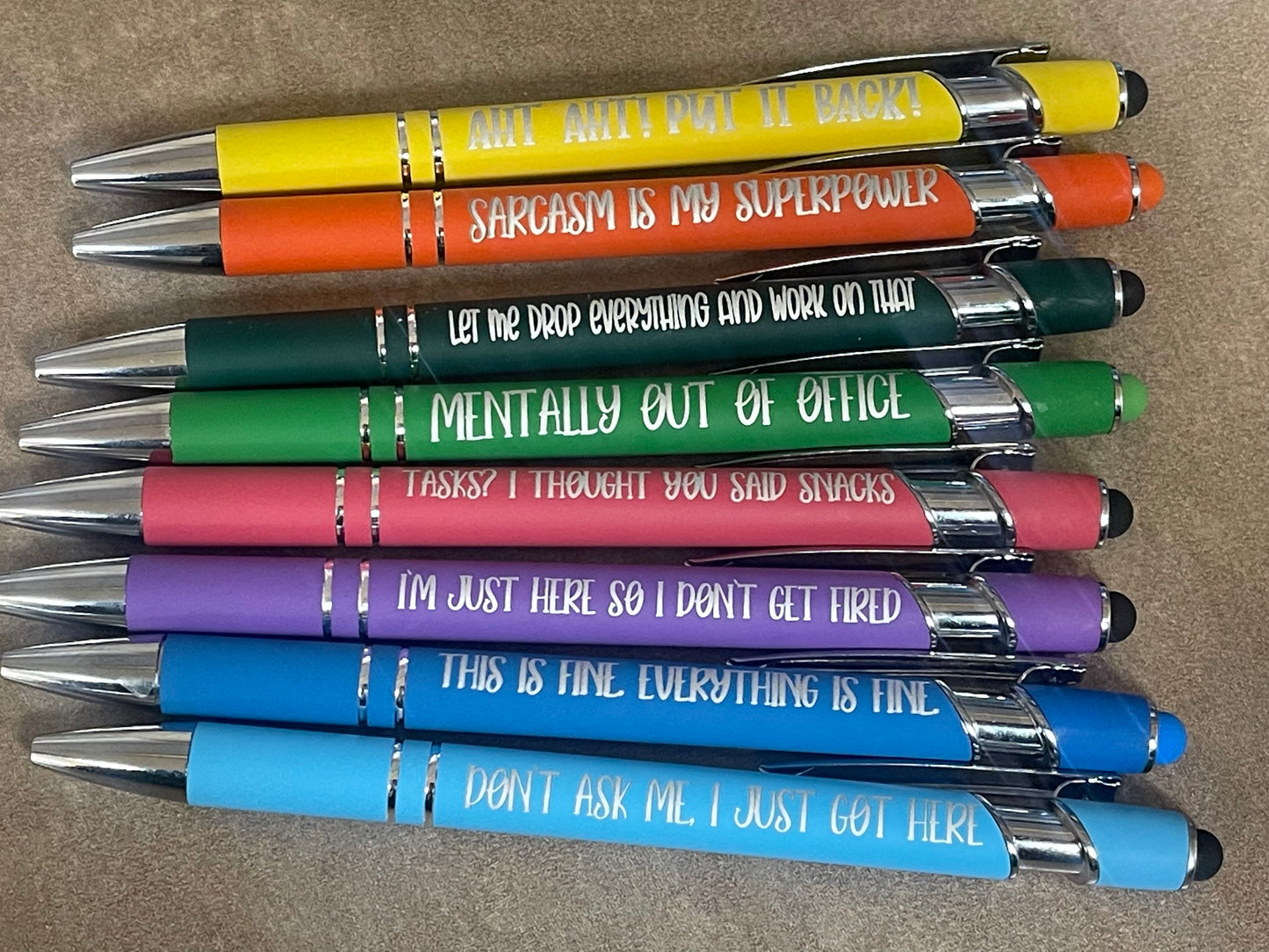 Stack of pens with humorous text on a brown surface