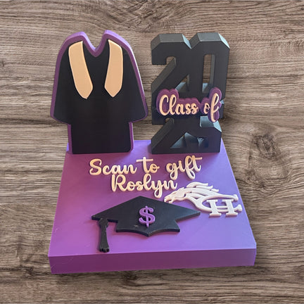 A 3D printed display stand with graduation-themed elements, including a graduation cap and gown, and personalized text areas for a name and school mascot or initials. The stand is in purple and black colors with a 'Scan to gift' text feature.