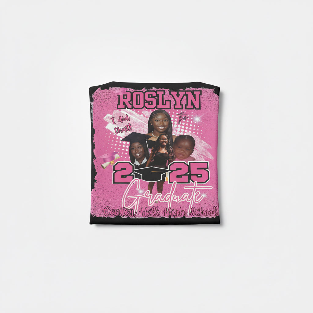 Pink graduation-themed shirt with text and images of people, held against a brick wall.