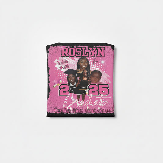 Pink graduation-themed shirt with text and images of people, held against a brick wall.