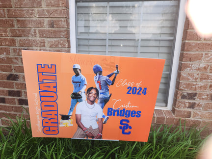 An orange yard sign with a photo of a graduate in a white shirt, featuring the text 'GRADUATE' and 'Class of 2024', along with the name 'Bridges' and the school logo 'SC'.