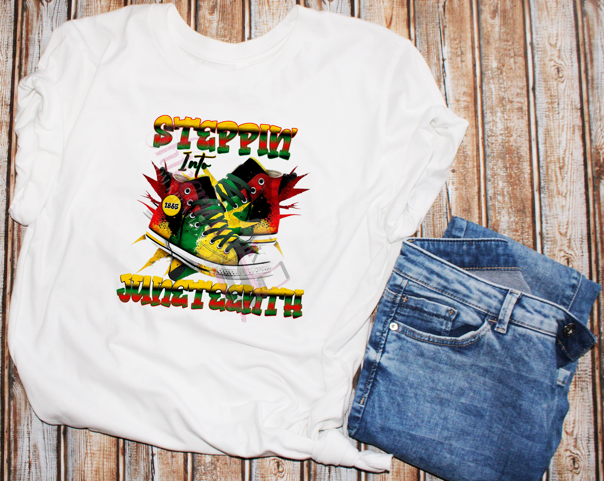 A white t-shirt with a graphic print featuring the text 'STEPPIN' INTO FREEDOM - JUNETEENTH' and images of sneakers, denoting a theme related to the Juneteenth holiday.