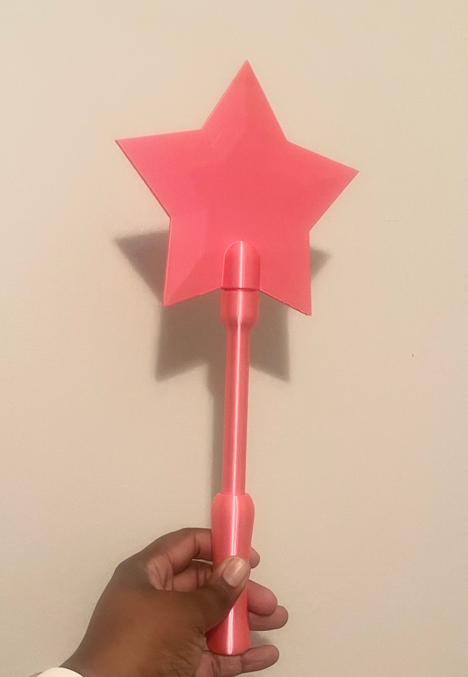Hand holding a pink star-shaped tap to pay wand against a beige background