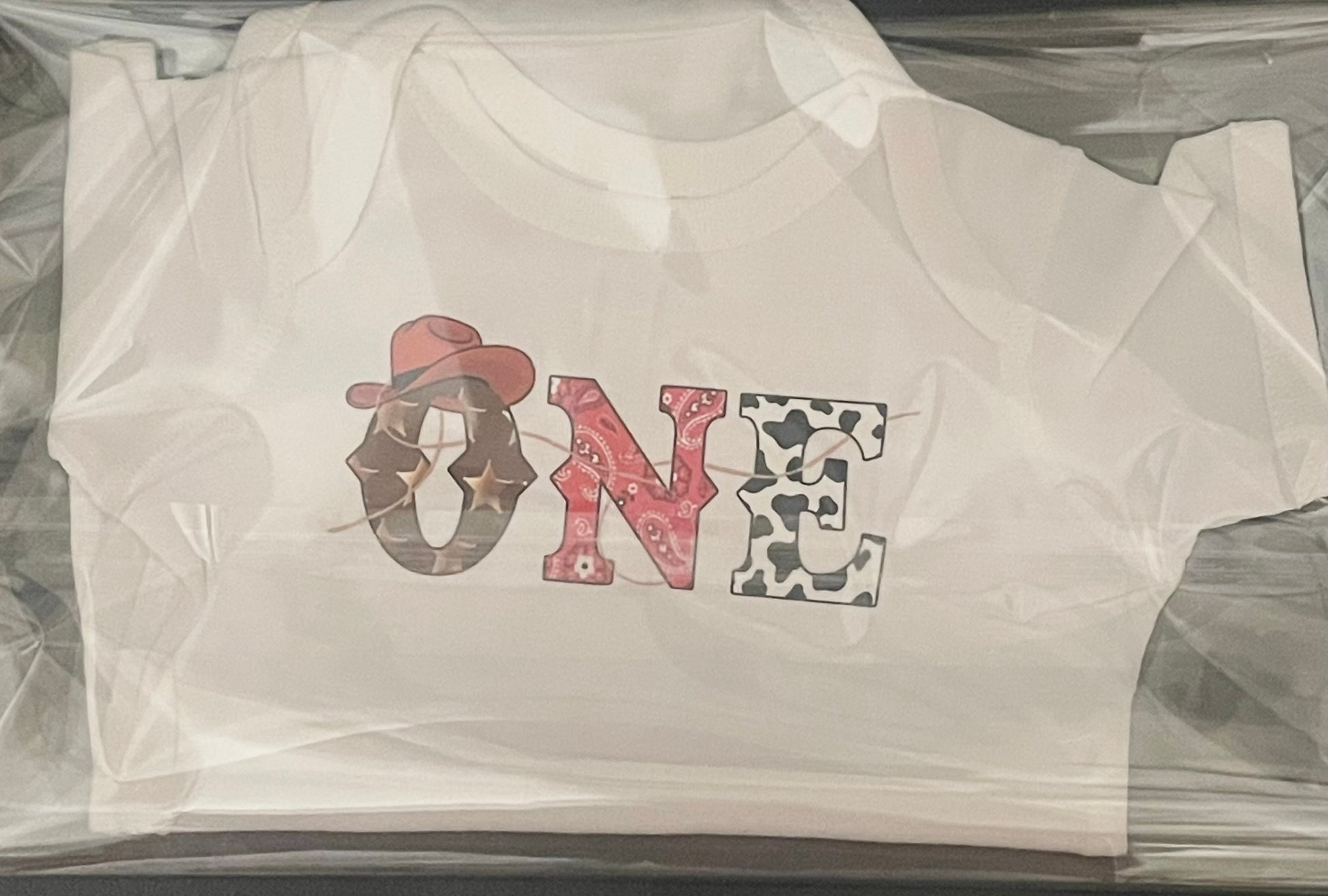 White t-shirt with 'ONE' design in cowboy hat and star pattern.