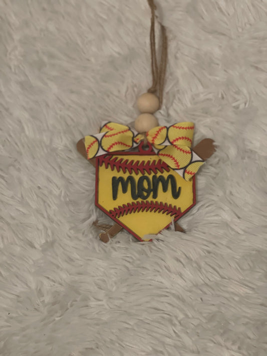A softball-themed car charm with the word 'mama' written in the center, crafted from wood, displayed on a furry surface.
