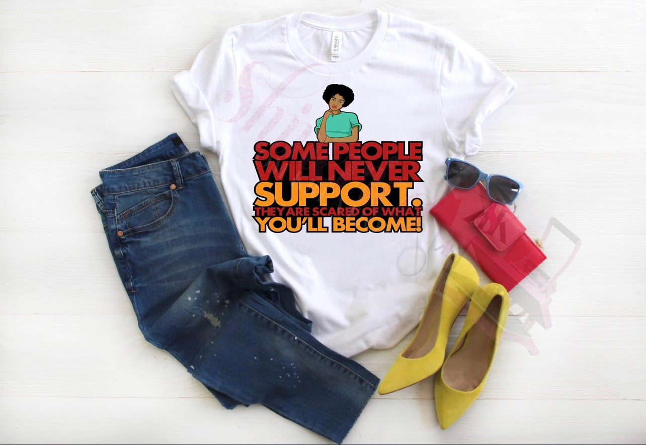 A white t-shirt with a graphic print of a woman and the text 'Some people will never support you. They are scared of what you'll become.